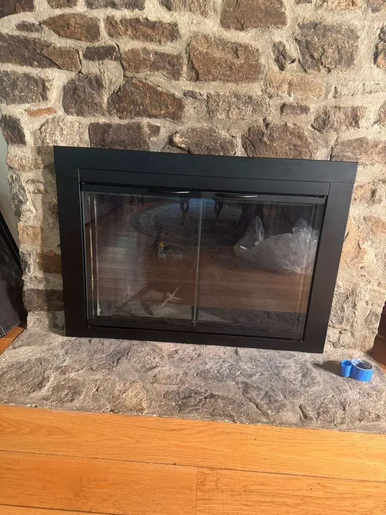 A black glass fireplace door set into a fieldstone fireplace, with a stone hearth below it.